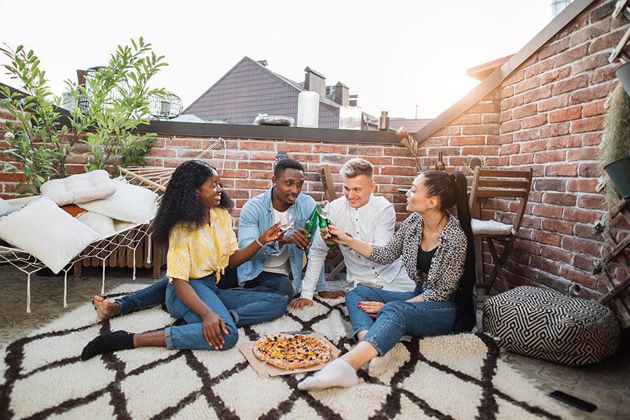 Personal Insurance - Couples on a Rooftop Deck, Brick Walls Around Them, Sitting on an Outdoor Rug Eating Pizza